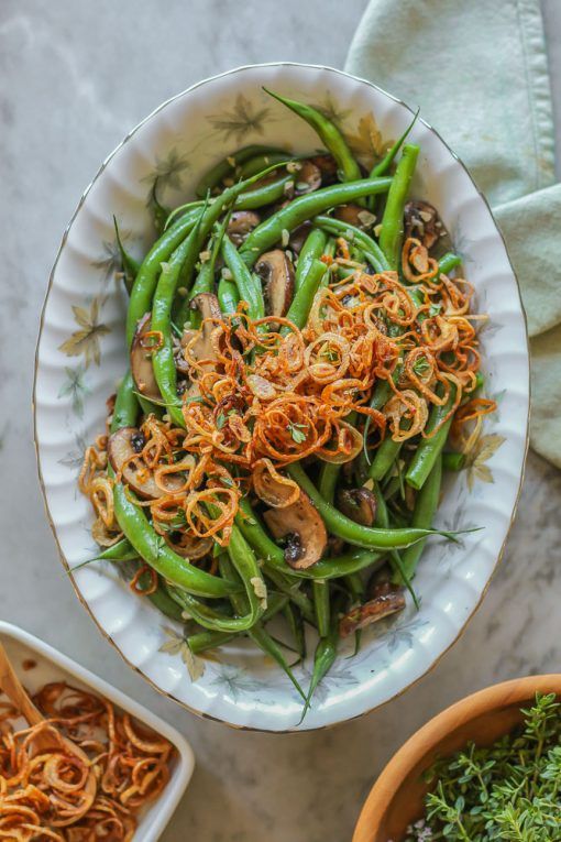 a white bowl filled with green beans covered in onion sprinkles and mushrooms