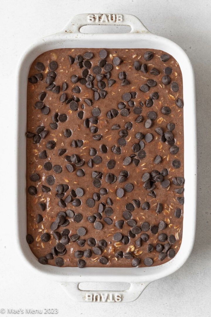 chocolate cake in a white baking dish with chocolate chips on the top and brownie crumbs on the bottom