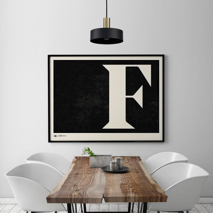 a dining room table with white chairs and a framed letter f on the wall above it