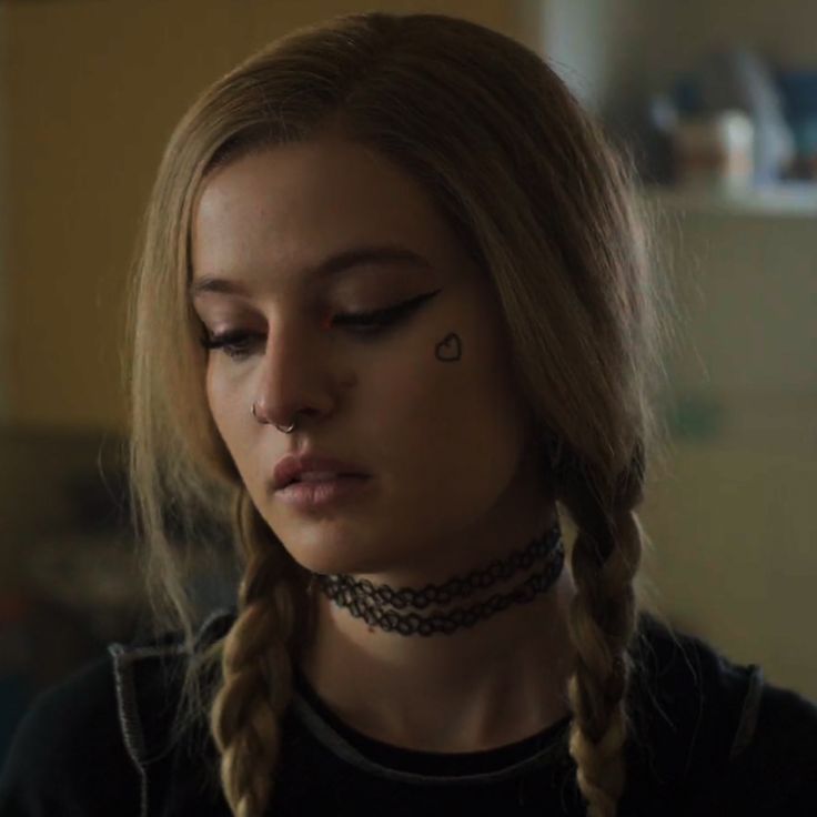 a woman with braids and piercings on her nose looks down at the camera