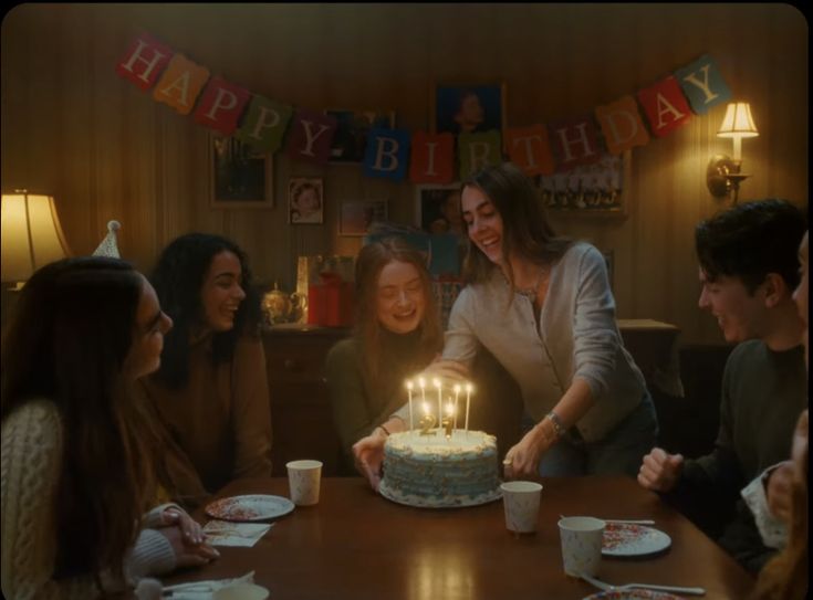 a group of people sitting around a table with a birthday cake on top of it