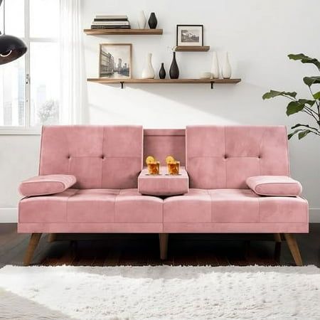 a pink couch sitting in front of a window next to a white rug on top of a wooden floor