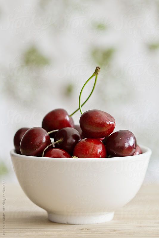 a white bowl filled with cherries on top of a wooden table