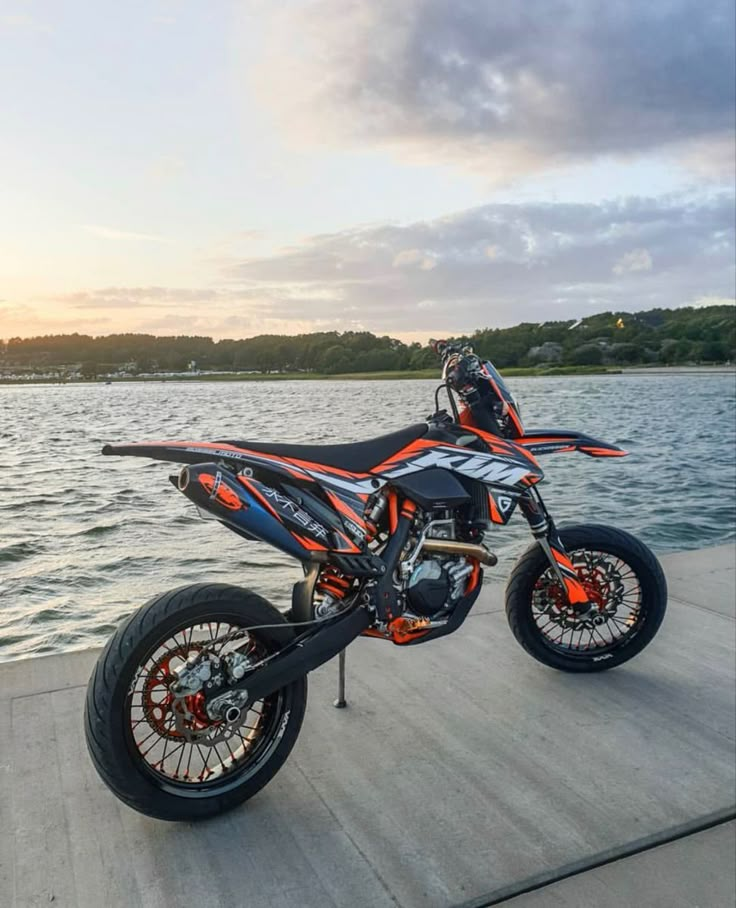 a dirt bike parked on top of a wooden platform next to the water at sunset