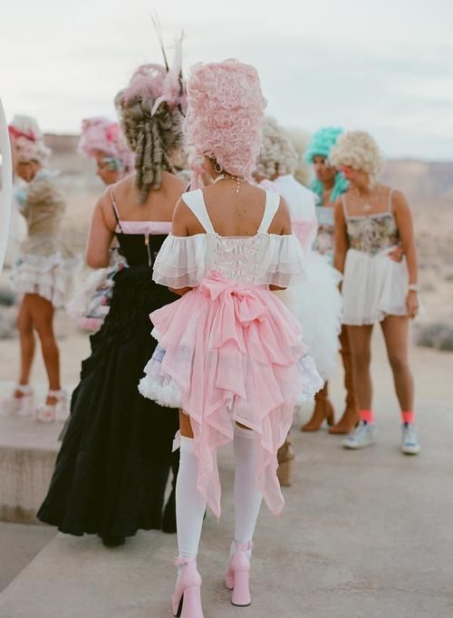 a group of women in dresses and wigs walking down the street together with one woman wearing pink hair