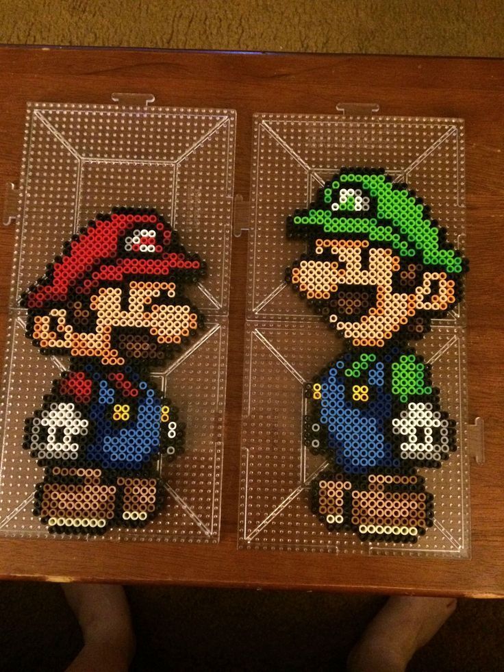 two pixel art pictures of mario and luigi in different colors on a wooden table with a person standing next to them