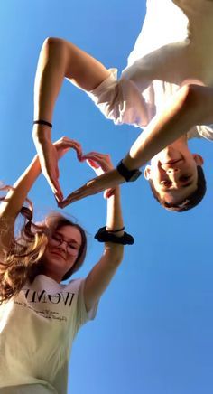 two people making a heart shape with their hands while standing in the air against a blue sky