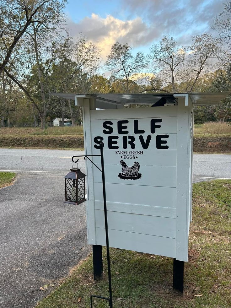 a sign that says self serve on it in front of a road with trees and grass