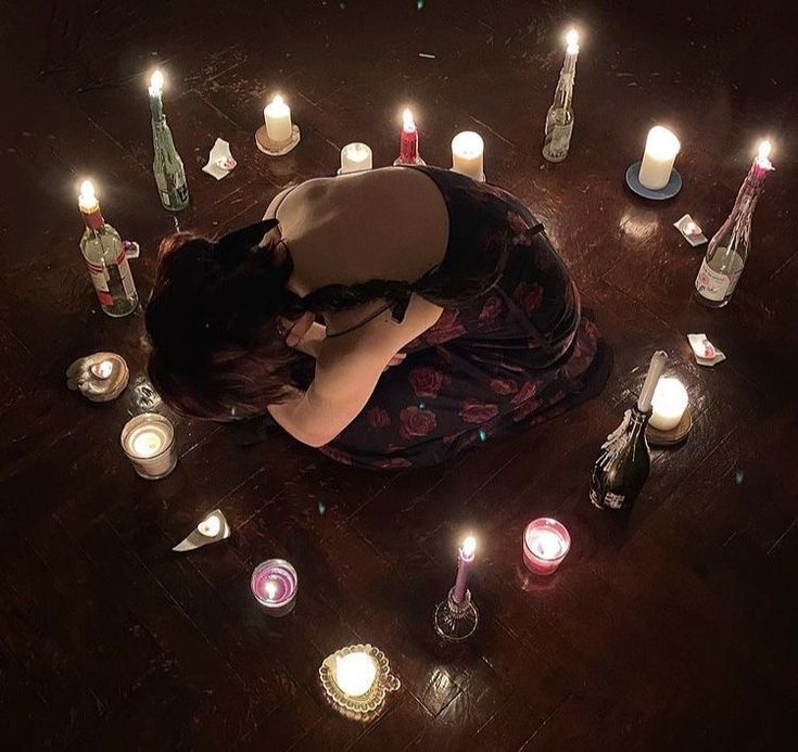 a woman is laying on the floor surrounded by candles and glass bottles, with her head in her hands