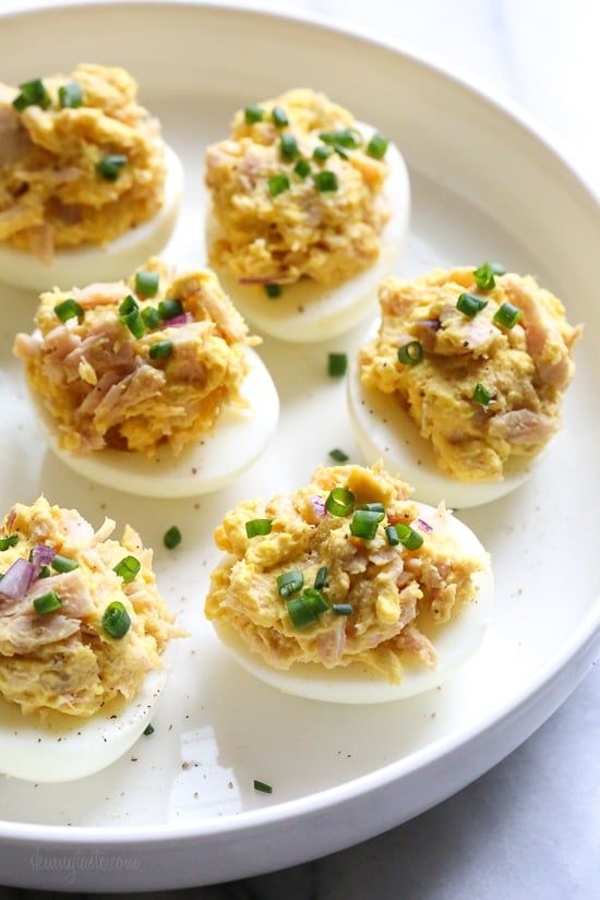 several deviled eggs with various toppings on a white plate