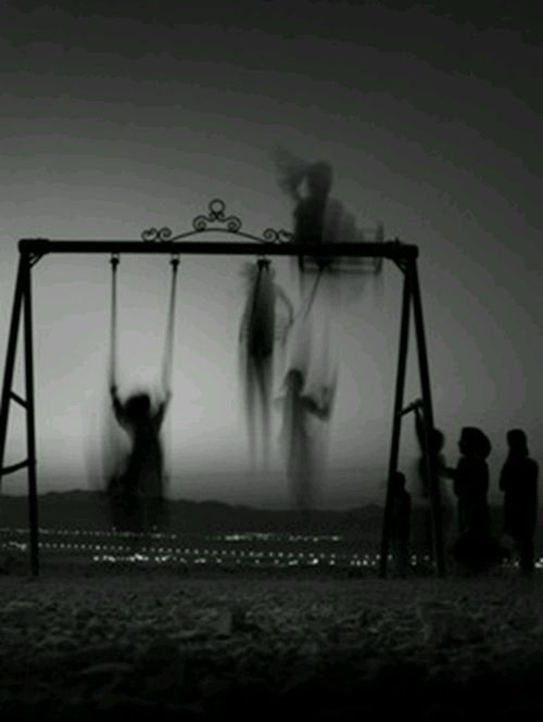 several people standing around a swing set on the beach at night with clouds in the sky