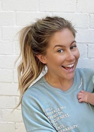 a woman holding a baby in her arms and smiling at the camera while wearing a t - shirt with words on it