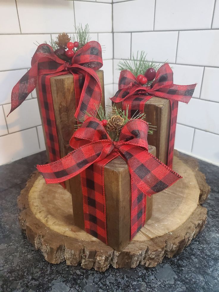 three wooden blocks with red and black plaid bows on them sitting on top of a tree stump