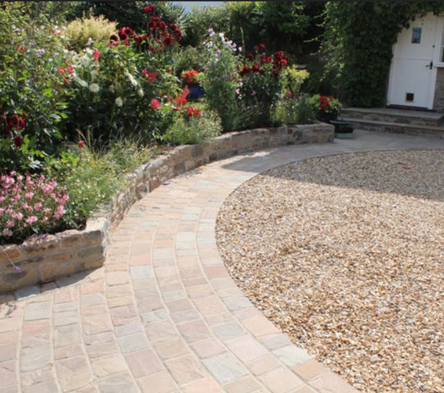 a brick walkway in front of a house with lots of flowers and plants around it