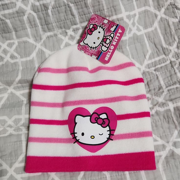 hello kitty beanie hat with pink and white stripes on it, sitting on a bed