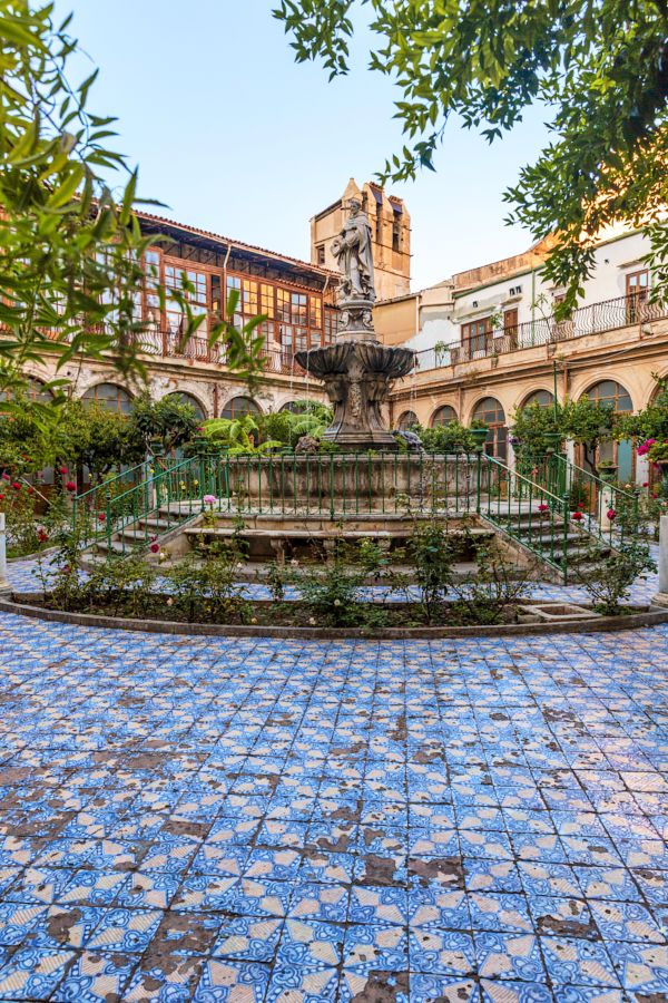 a fountain in the middle of a courtyard surrounded by trees and buildings with blue tiles on it