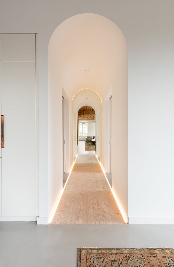 an arched hallway with white walls and wood flooring is illuminated by led lights on either side of the doorway