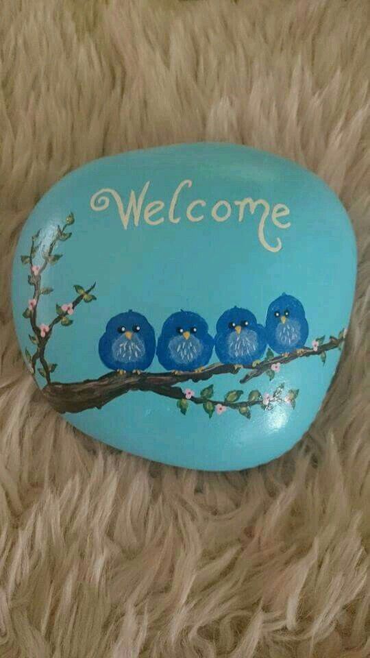 a painted rock with birds on it and the words welcome written in white lettering, sitting on a furry surface