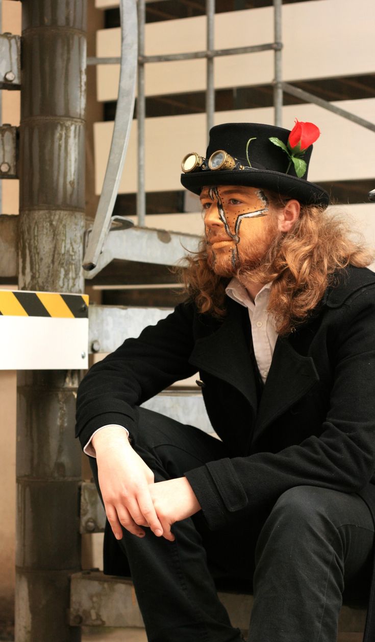 a man with long hair wearing a top hat and black suit sitting on a bench