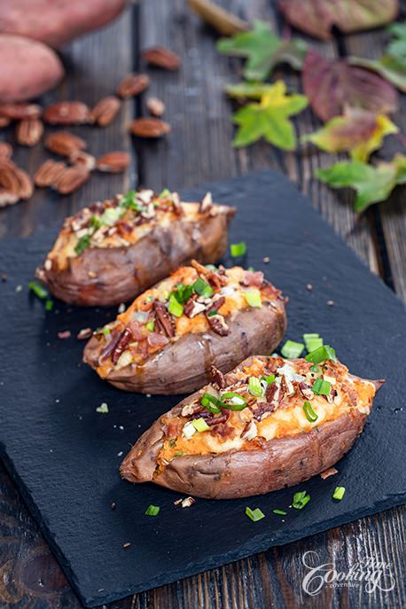 three baked sweet potatoes with toppings on a slate platter next to pecans