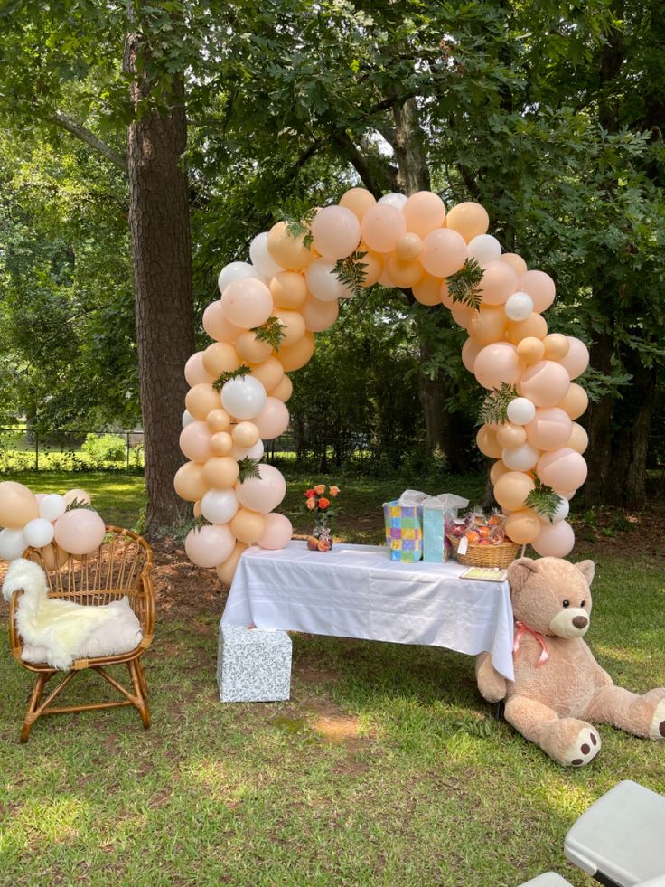 a teddy bear sitting in front of a table with balloons on it and a chair