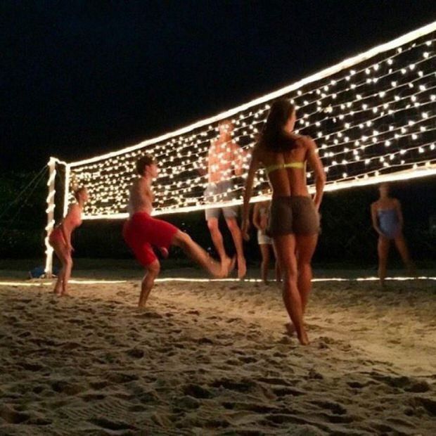 people are playing volleyball on the beach at night with lights in the background and an ad that says volleyball net out of the string lights for night time volleyball games