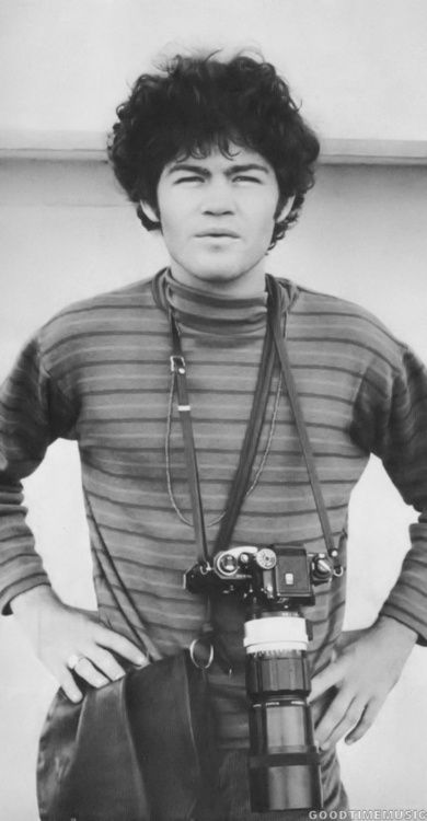 black and white photograph of a man holding a camera with his hands on his hips