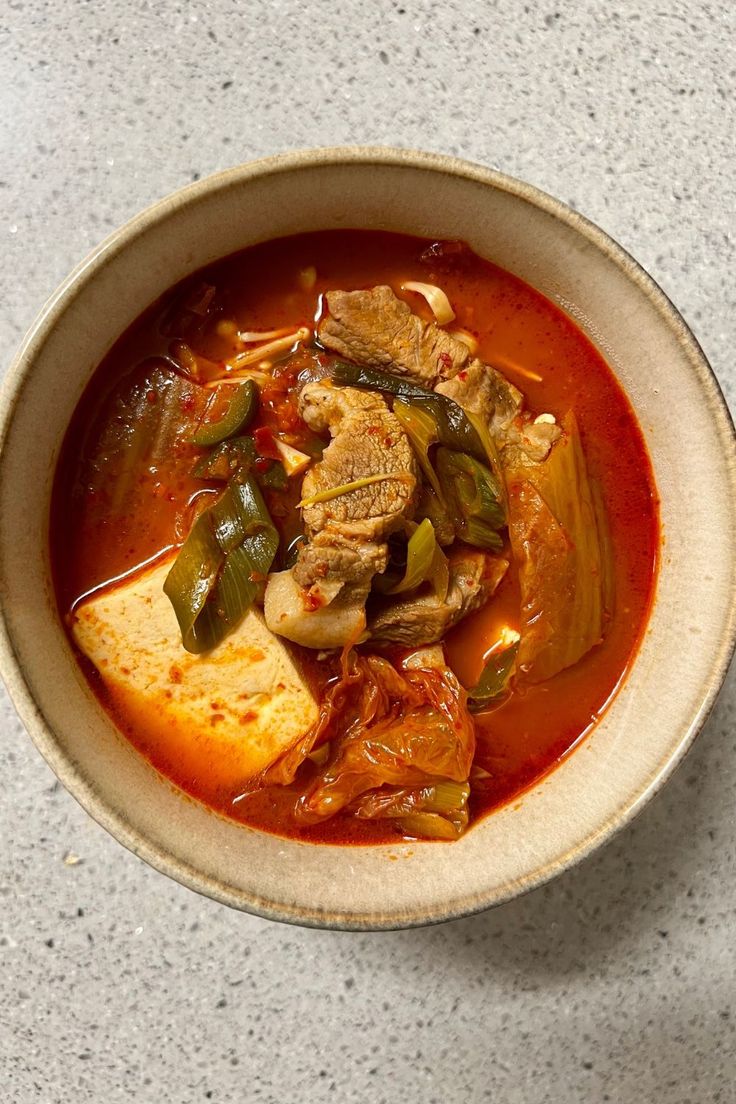 a bowl filled with meat and vegetables on top of a white countertop next to a cup of coffee