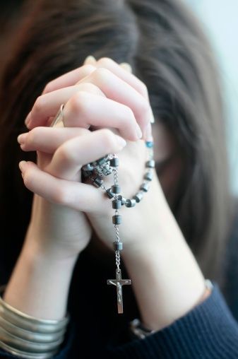 a woman holding her hands to her face while wearing a rosary