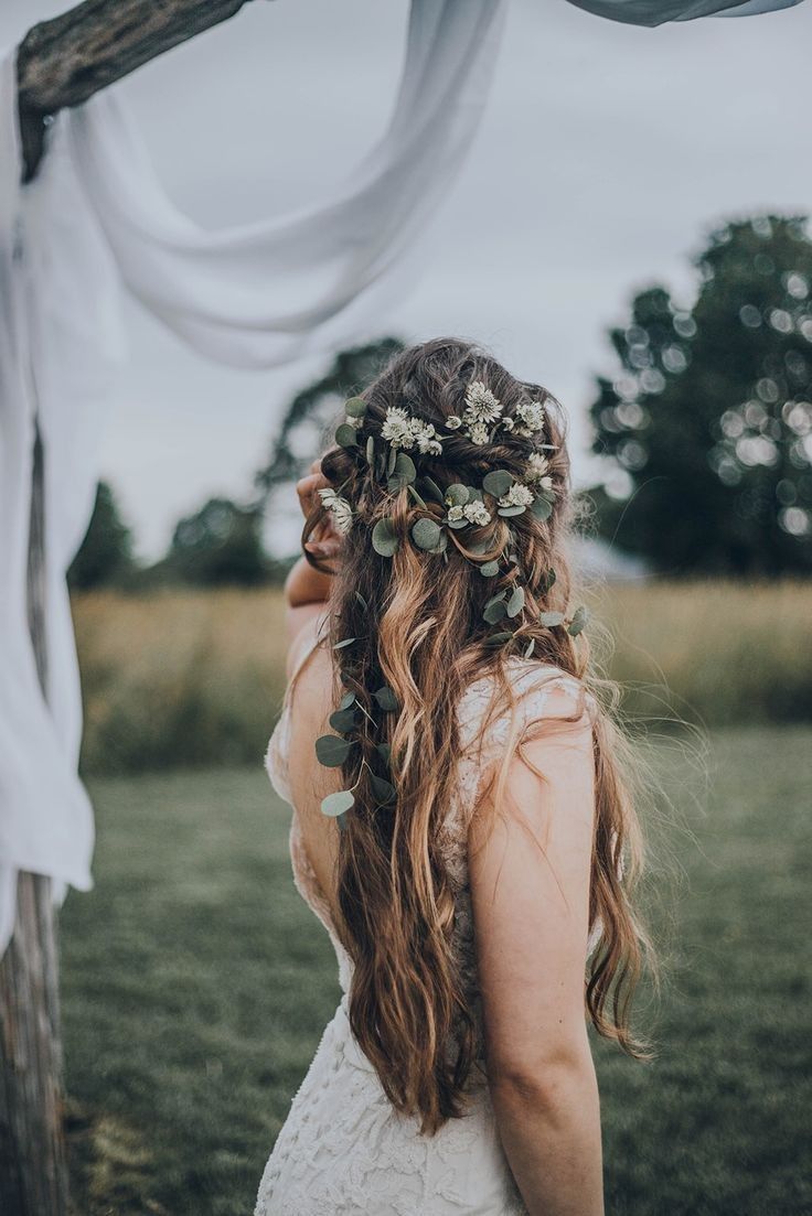 a woman with long hair and flowers in her hair is standing under an arbor outside