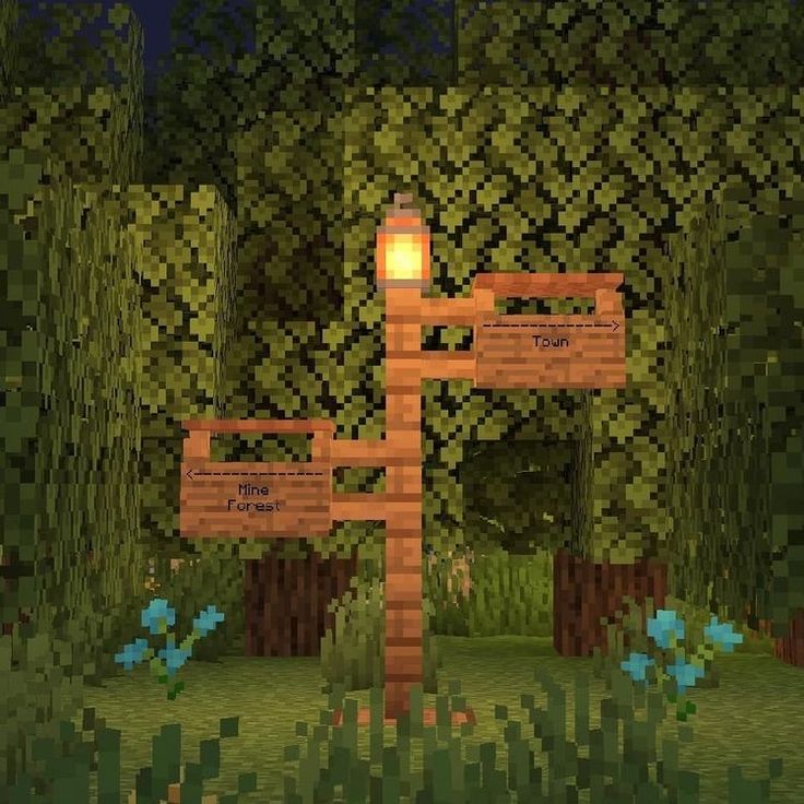 a wooden sign sitting in the middle of a lush green forest at night with lights on