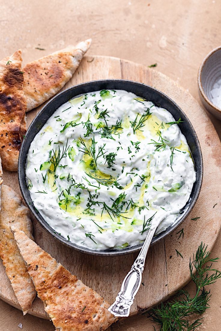 a bowl of white dip with pita bread and dill sprigs on the side