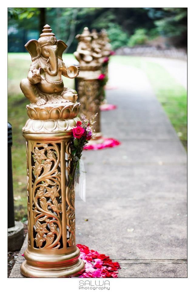 some gold statues sitting on the side of a road next to red flowers and greenery