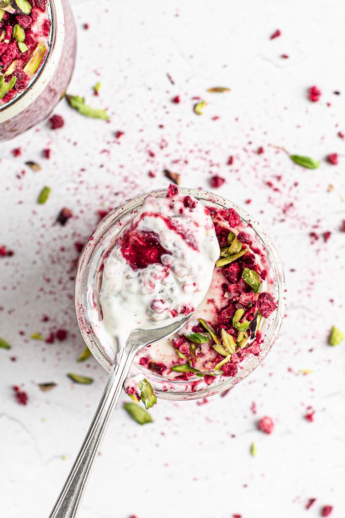 two glasses filled with yogurt and topped with pistachios on a white surface