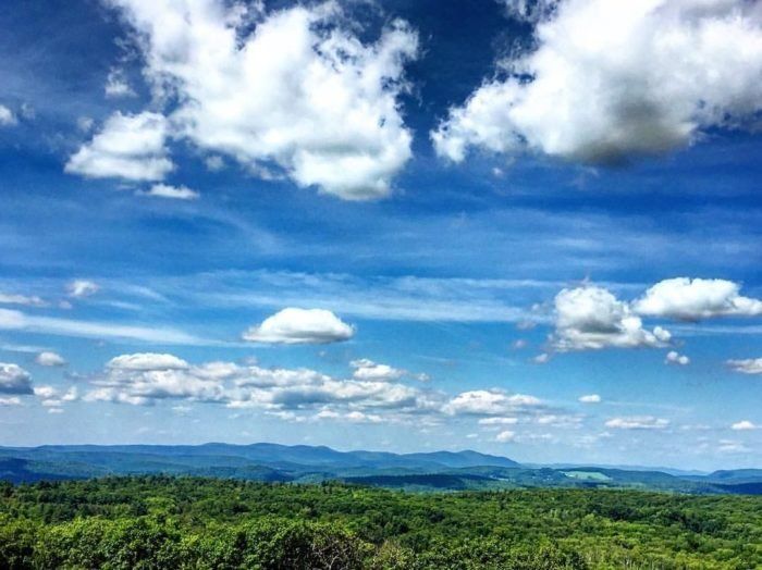 a scenic view of mountains and trees under a blue sky with white clouds in the distance