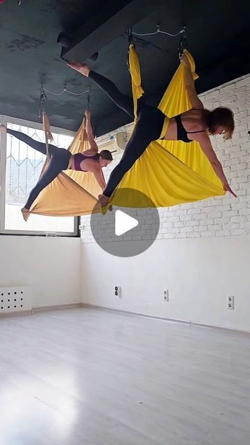 two people are hanging upside down on hammocks in an empty room with white brick walls