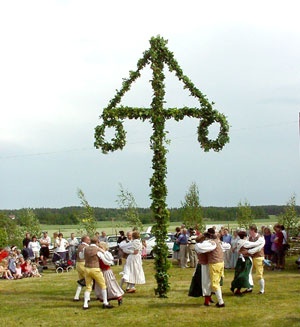 a group of people dancing around a cross made out of vines and leaves in a field