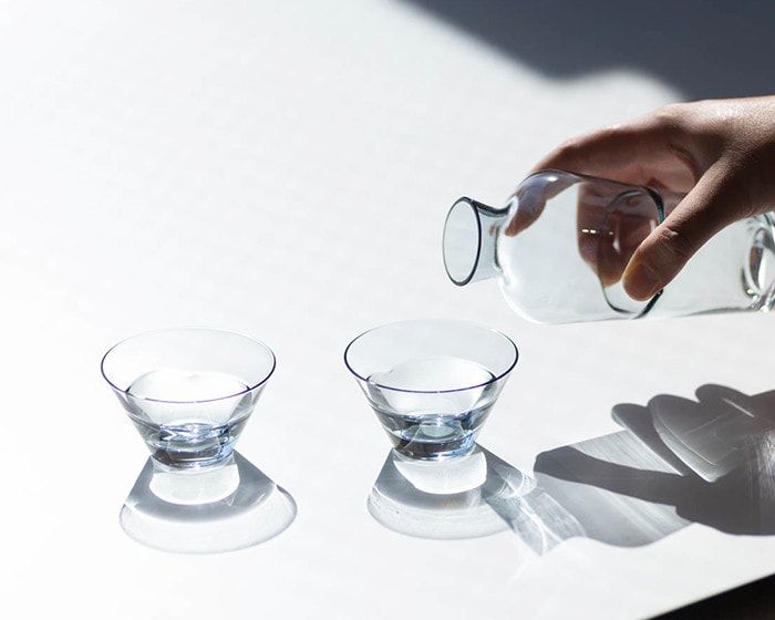 a person pouring water into two glasses on a table with shadow from the sun shining on them