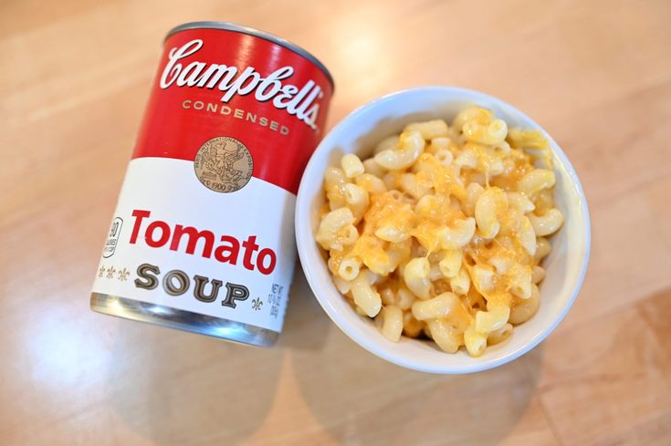 a bowl of macaroni and cheese next to a can of soup on a table