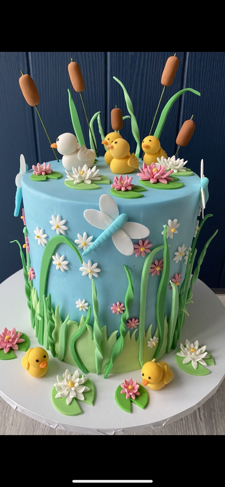 a cake decorated with fondant flowers and ducks in the pond on top of it