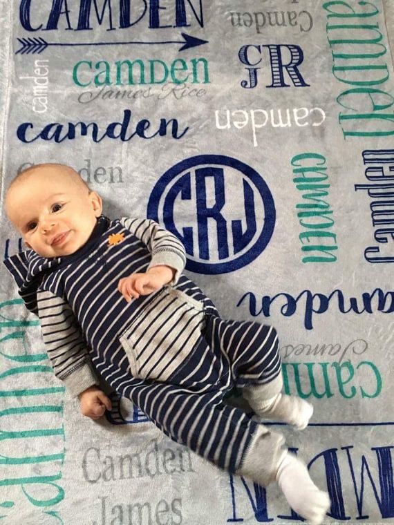 a baby laying on top of a blanket covered in letters and names with a monogrammed background