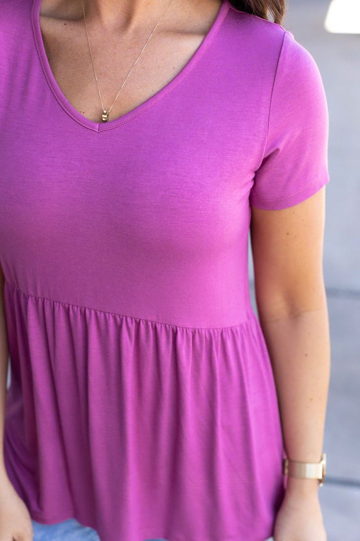 Feel gorgeous in the Sarah Ruffle Short Sleeve Top in a vibrant orchid shade! This delightful top combines a sweet, classic design with a playful ruffle detail, making it a standout piece in any wardrobe. Its unique shape strikes a balance between baby-doll and peplum, offering a fit that flatters every figure. Made from a soft and stretchy blend of 95% rayon and 5% spandex, this top promises comfort and flexibility for all-day wear. Fabric Composition: 95% rayon, 5% spandex for a comfortable an Feminine Pink Solid Color Tops, Chic Pink Solid Color Top, Chic Solid Pink Top, Flowy Solid Color Tops, Chic Purple Flowy Top, Purple V-neck Solid Color Top, Purple V-neck Solid Top, Purple V-neck Top, Pink Ruffle Hem Top For Day Out