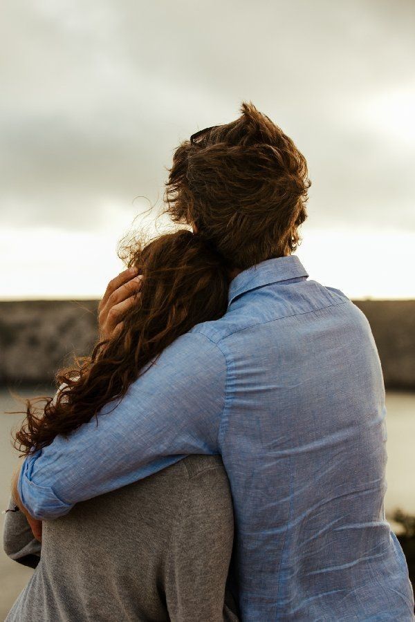 two people hugging each other in front of a body of water