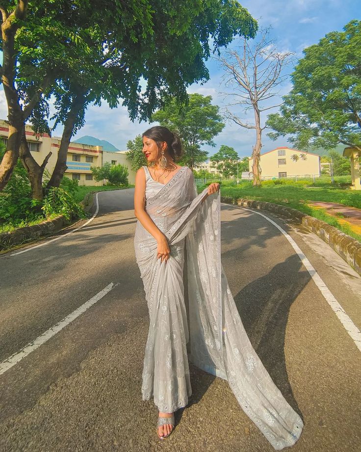 a woman standing on the side of a road wearing a sari and holding a shawl