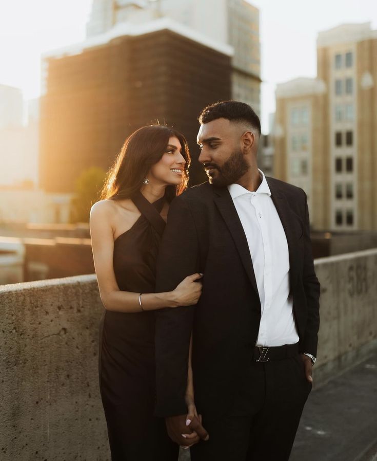 a man and woman standing next to each other on a bridge in front of tall buildings