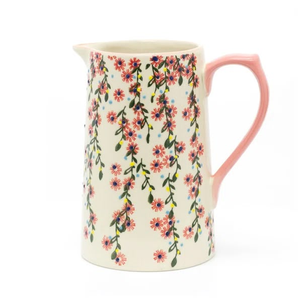 a white and pink flowered pitcher with orange handles on a white background is shown