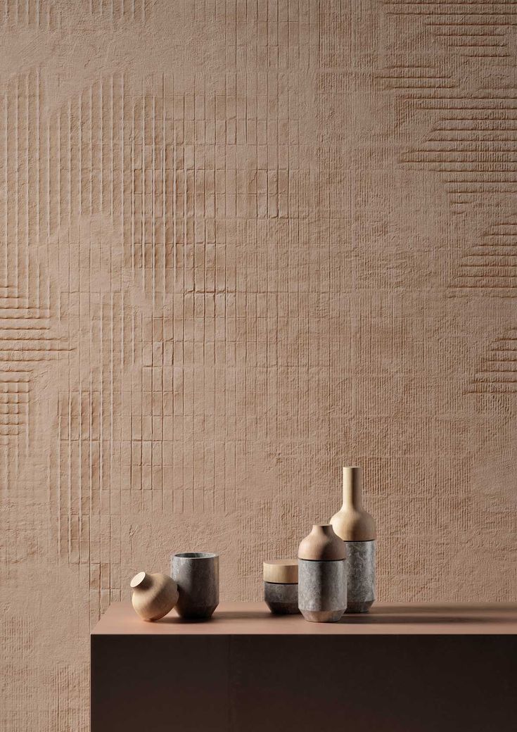 three vases sitting on top of a wooden table next to a wall with a textured background