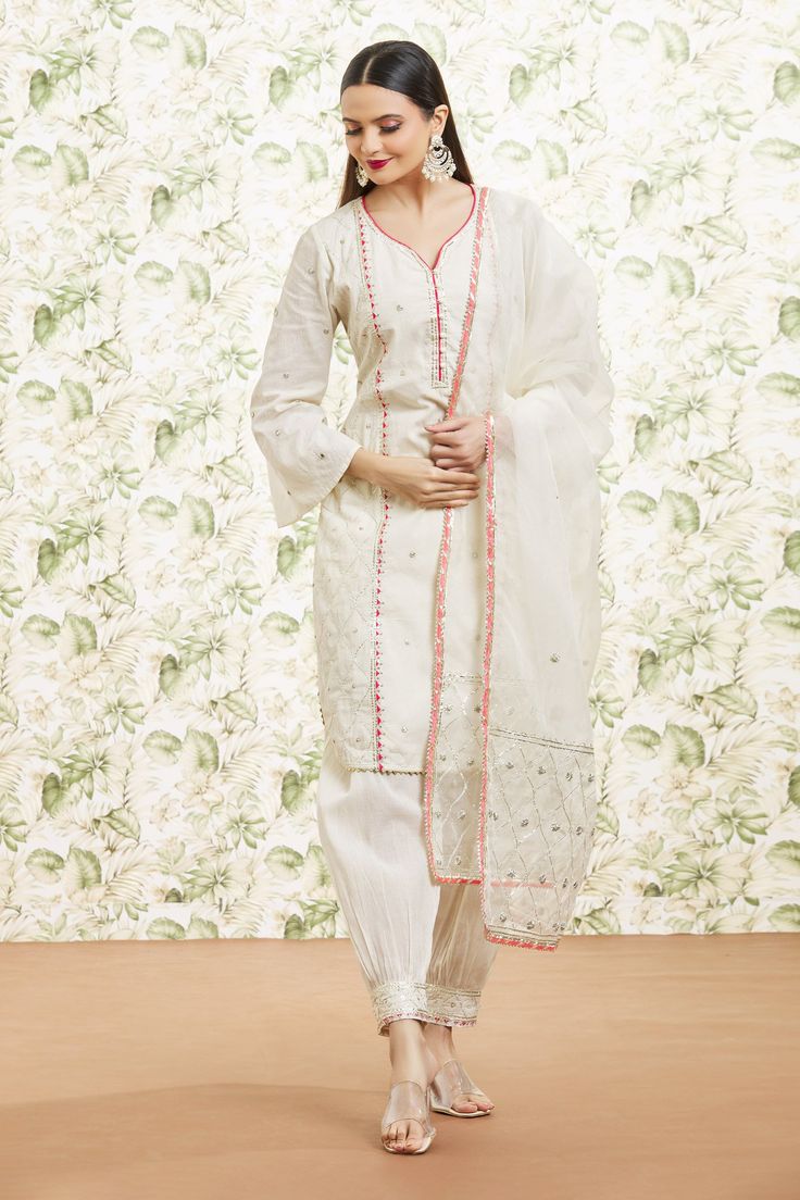 White cotton kurta with bell sleeves, all over mirror, resham work, gota sequin, bead embroidered side panels and contrast applique details. Paired with farzi pant with embroidered border and dupatta with gota embroidered border.
Components: 3
Pattern: Embroidered
Type Of Work: Resham, Sequin, Beads, Gota and Mirror Work
Neckline: Leaf Neck
Sleeve Type: Bell Sleeves
Fabric: Cotton, Dupatta: Organza, Lining: Cotton
Color: White
Other Details: 
Cut work hem details
Curved kurta hem
Contrast pink b Unstitched Cotton Suit With Mirror Work, Cotton Palazzo Set With Straight Kurta And Mirror Work, Festive Cotton Unstitched Suit With Mirror Work, Cotton Palazzo Set With Gota Work And Long Sleeves, Cotton Long Sleeve Palazzo Set With Gota Work, Cotton Unstitched Suit With Mirror Work For Eid, Long Sleeve Cotton Silk Salwar Kameez With Mirror Work, Cotton Salwar Kameez With Mirror Work For Eid, Festive Cotton Unstitched Suit With Gota Work