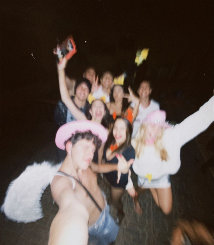 a group of young people posing for a photo at night with their arms in the air