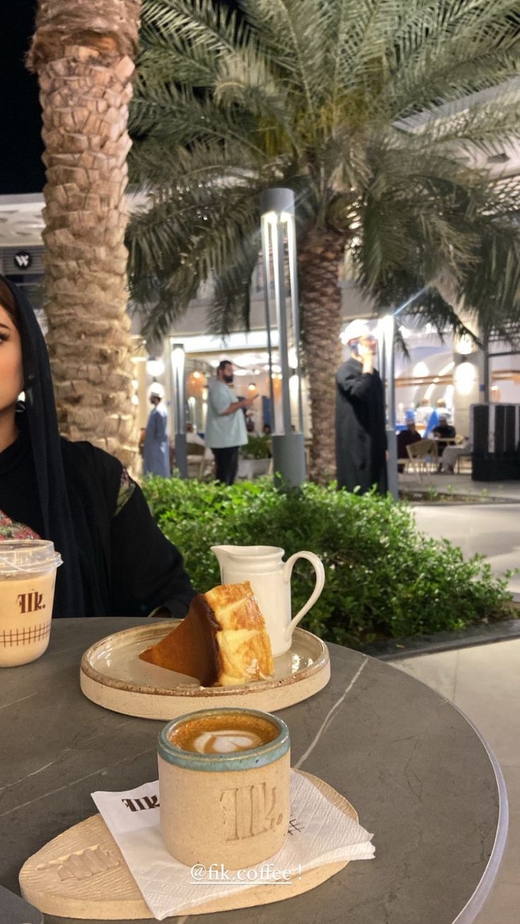 a woman sitting at a table in front of a cup of coffee and some food